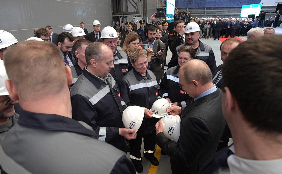 Vladimir Putin talks with shipyard workers and signs their helmets during a visit to the Severnaya Verf Shipyard.
