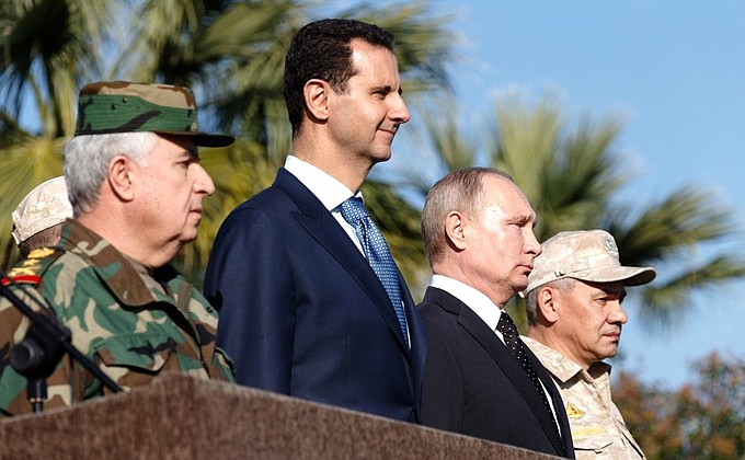Во время посещения авиабазы Хмеймим в Сирии. С Президентом Сирии Башаром Асадом (слева) и Министром обороны России Сергеем Шойгу (справа).